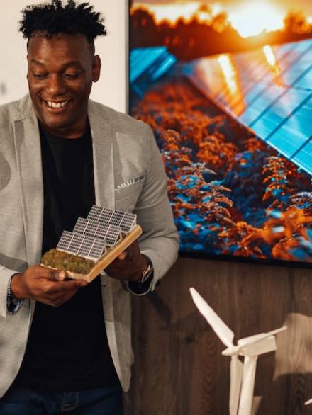 Portrait of smiling multicultural ecology expert standing at boardroom at corporate office and having presentation with solar panel miniature in hands.Environmentalist presenting innovative technology